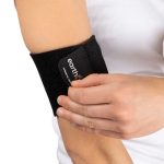 A person in a white shirt adjusts the Earthing Band around their forearm, just below the elbow.