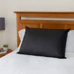 A rectangular black Earthing Pillow Cover centred on a bed with a wooden headboard.