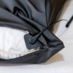 A close-up of the black Earthing Pillow Cover with a zippered cushion and a small black electronic sensor attached to the edge, partially exposing the white inner pillow.