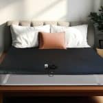 A black Earthing® Grounding Mattress Cover - King Size with an attached grounding lead and plug resting on a bed.