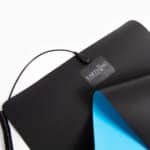 A partially rolled-up Universal Earthing Mat Pack, black with a blue underside and labeled EARTHING, features an attached cord and rests on a white surface.