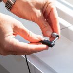 Close-up of hands connecting a black power adapter plug into the Earthing Grounding Rod, a small cylindrical device, near a bright window as sunlight streams in—evoking the stable energy connection provided by grounding.