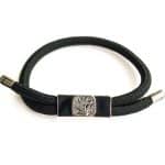 The EarthBand PEMF Bracelet from BeGrounded features a rectangular metal centerpiece with a tree design on a black cord. Silver-tone metal caps finish the ends, elegantly showcased on a pristine white background.