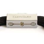 A close-up of the EarthBand PEMF Bracelet from BeGrounded reveals its minimalist metallic clasp engraved with EARTHBAND, featuring two circular accents flanking a central loop. The textured black material not only exudes style but also provides subtle wellness benefits through PEMF technology.