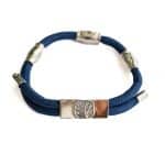 The EarthBand PEMF Bracelet from BeGrounded is a sleek blue rope bracelet with silver accents, a central silver plate embossed with a tree design, and features PEMF technology. It has multiple strands and lobster clasp closures.