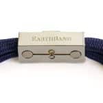 Close-up of a metallic clasp on the EarthBand PEMF Bracelet by BeGrounded, with engraved EARTHBAND text on a navy braided band. It features circular designs, a small stone, and is set against a neutral background.