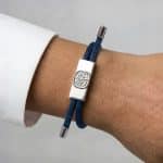 An Earthband PEMF Bracelet in navy blue on a wrist, featuring a rectangular silver centrepiece with an embossed tree design and silver end caps.