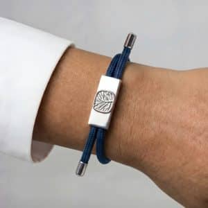 Earthband PEMF Bracelet featuring a rectangular silver-tone metal charm with an embossed leaf design on a black cord, worn on a wrist.