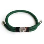 The EarthBand PEMF Bracelet from BeGrounded features a green braided band, silver metal clasp, and a decorative centerpiece engraved with a tree design, set against a plain white background.