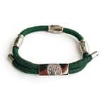 The EarthBand PEMF Bracelet from BeGrounded is a green braided cord bracelet with three silver cylindrical clasps and a central rectangular metal piece featuring a tree design, enhanced with subtle PEMF elements for wellness.