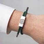 A dark green Earthband PEMF Bracelet featuring a rectangular silver-tone metal centre piece with an embossed tree design, worn on a wrist.