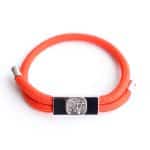 The EarthBand PEMF Bracelet from BeGrounded features a bright orange flexible band with metallic ends and a rectangular silver clasp showcasing a tree design in relief, serving as a focal point against the plain white background.