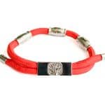The EarthBand PEMF Bracelet from BeGrounded features a red rope design with metallic tube clasps and a central rectangular piece engraved with a tree emblem, enhanced by PEMF technology.