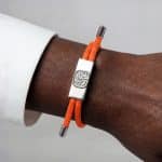 Bright orange Earthband PEMF bracelet featuring a rectangular metal centrepiece with an engraved tree design.