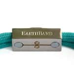 A close-up of a turquoise braided bracelet with a rectangular metal clasp engraved with the word EarthBand. The clasp is silver with gold accents and circular details.