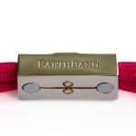 A close-up of a pink braided bracelet with a metallic clasp engraved with the word EARTHBAND on a white background.