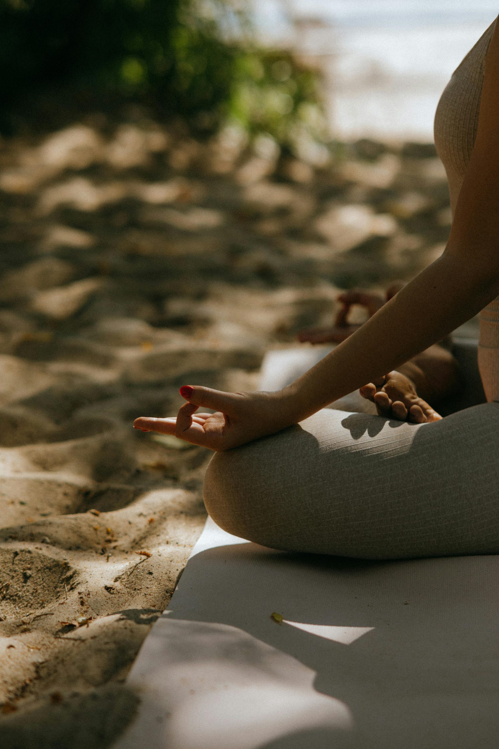 A person sits cross-legged on a yoga mat outdoors, practicing meditation with sunlight all around—an ideal moment to experience Portable Grounding Solutions for Travelling, surrounded by sandy ground and peaceful energy.