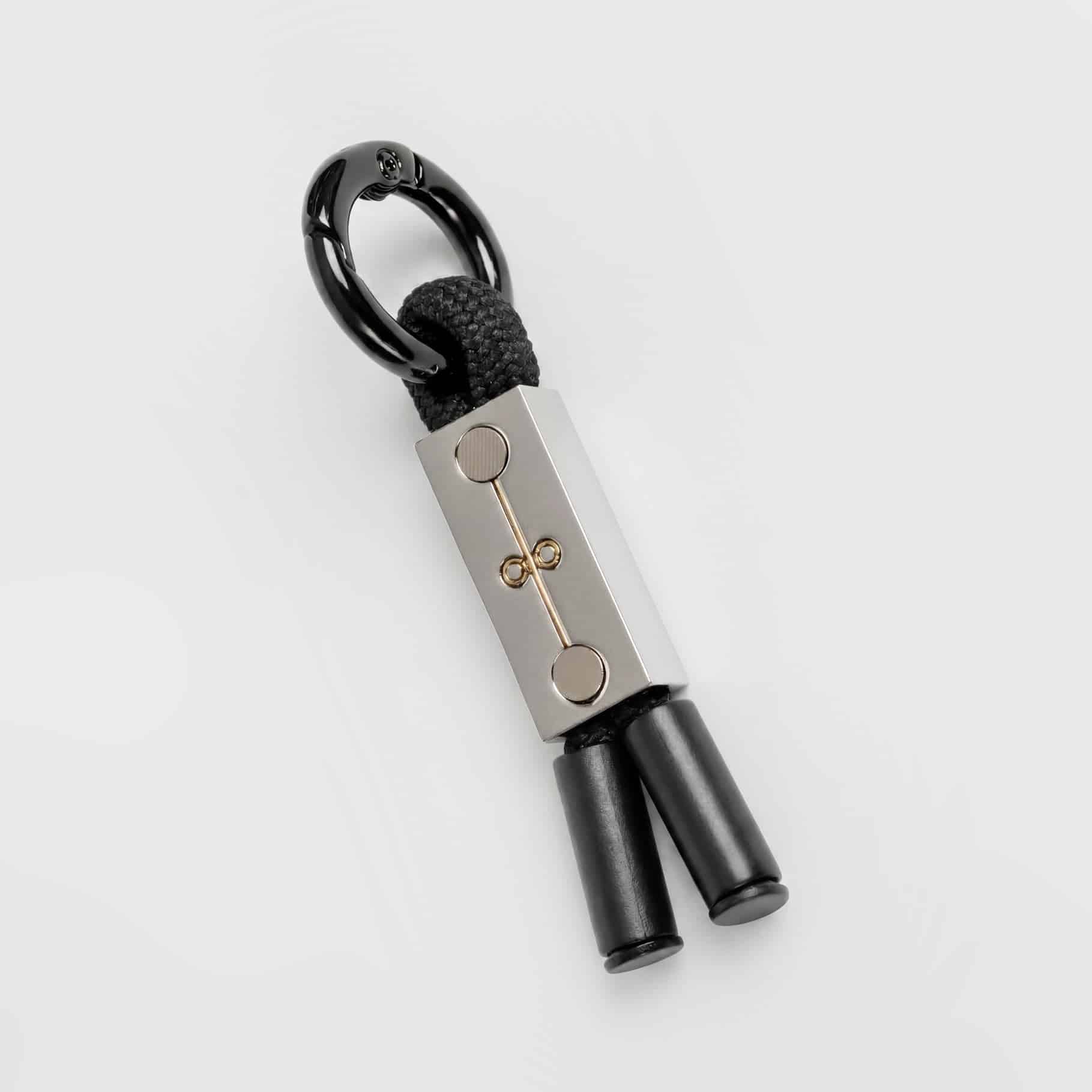 The Earthband For Pets is a modern PEMF keyring with a rectangular metal piece, minimalist design, black rope looped through it, two black cylindrical ends, and a black metal keyring.