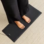 Bare feet standing on a rectangular black earthing mat with a lead attached.