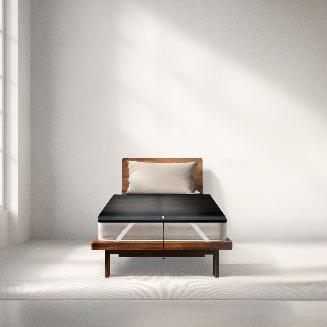 A mattress on a wooden bed frame with a black heating or cooling pad topper attached to the top.