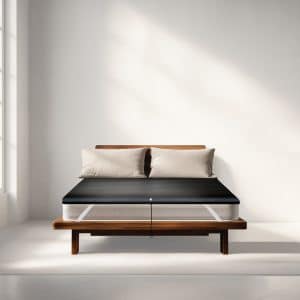 A white mattress on a wooden bed frame, covered by a black protective topper with a central strap.