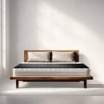 A wooden platform bed with a mattress and two beige pillows against a white wall.